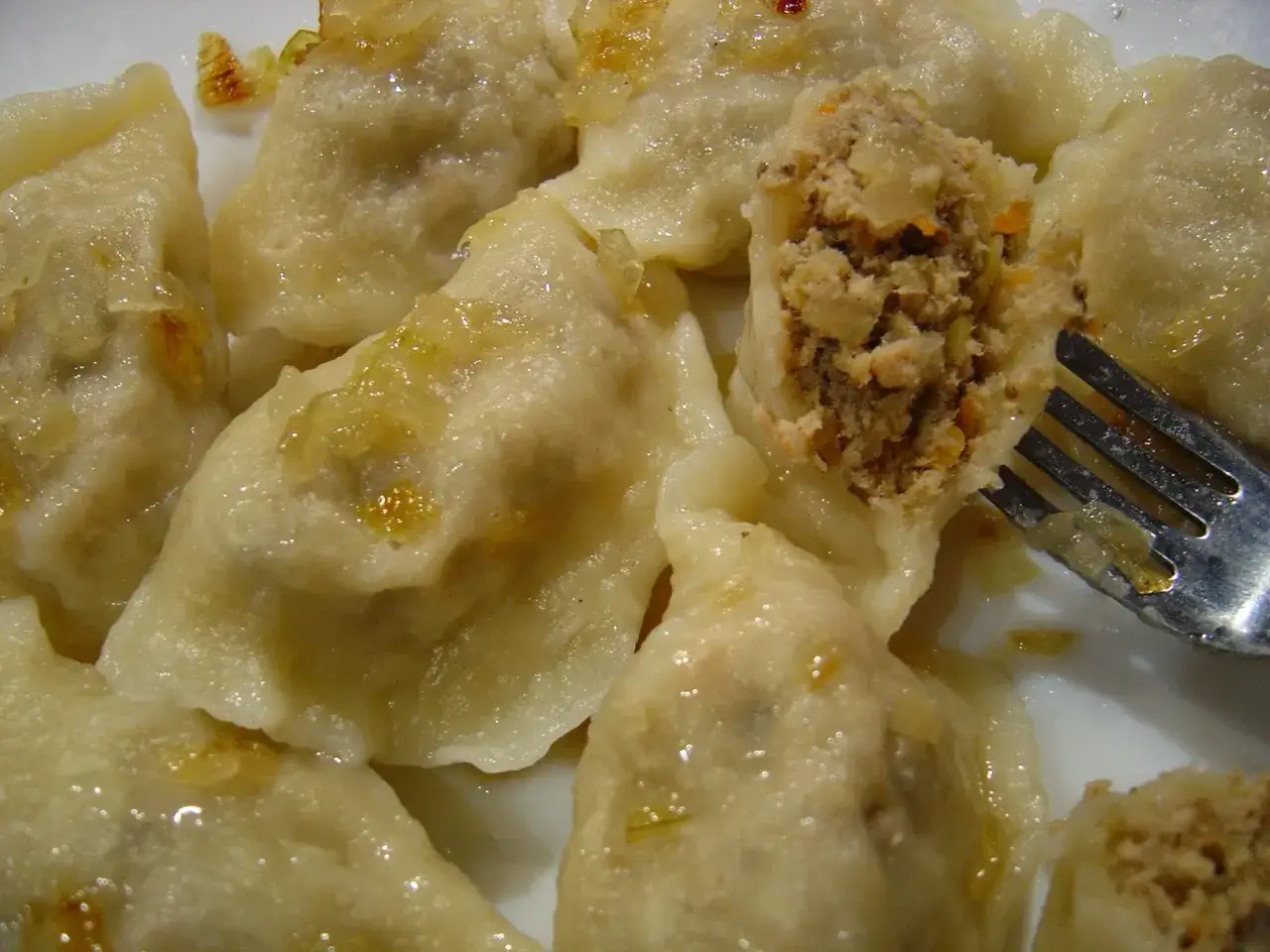 Pyszne pierogi z mięsem i kapustą, polane tłuszczem z cebulką. Jeden pier&oacute;g jest przekrojony, ukazując bogate nadzienie.