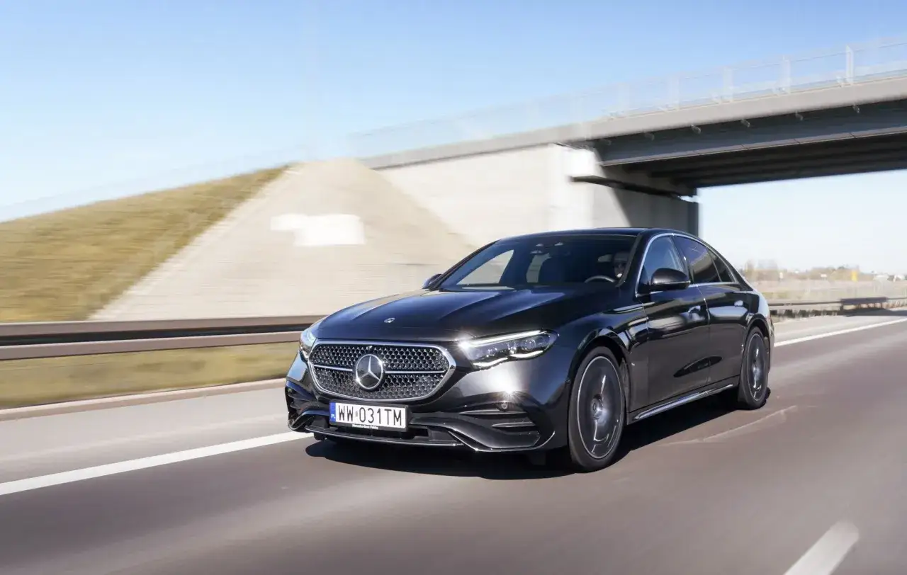 Elegancki, czarny Mercedes E220d sunie po autostradzie, podziwiając krajobraz pod błękitnym niebem.