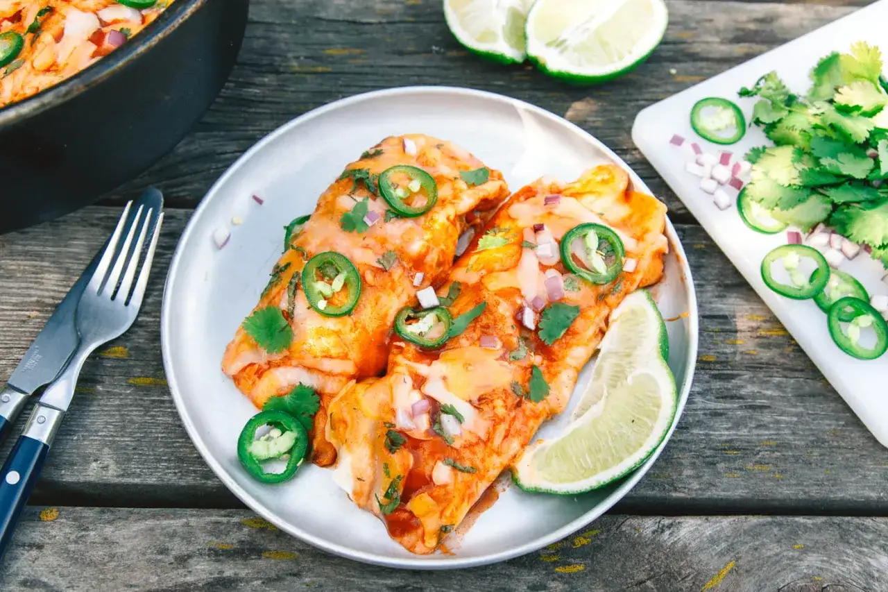Delicious dutch oven enchiladas, topped with jalapeños, cilantro, and red onion, served with lime wedges.