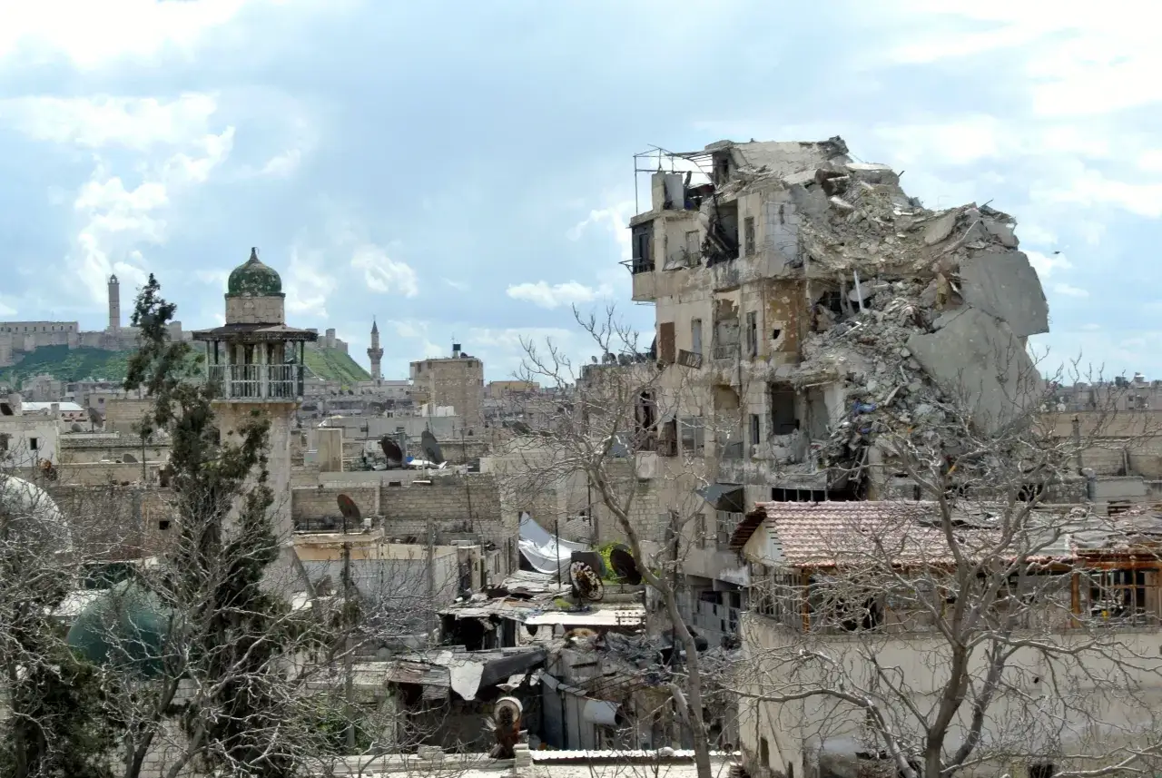 Zniszczone budynki i ruiny w mieście, z minaretami i kopułą w tle. Obraz sugeruje, czy w Syrii jest bezpiecznie.