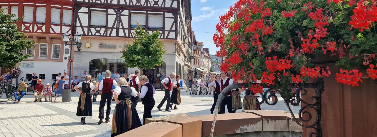 Tanzgruppe in Tracht belebt den Marktplatz. Viele Besucher genie&szlig;en die **Veranstaltungen heute in Tauberbischofsheim** bei strahlendem Sonnenschein.