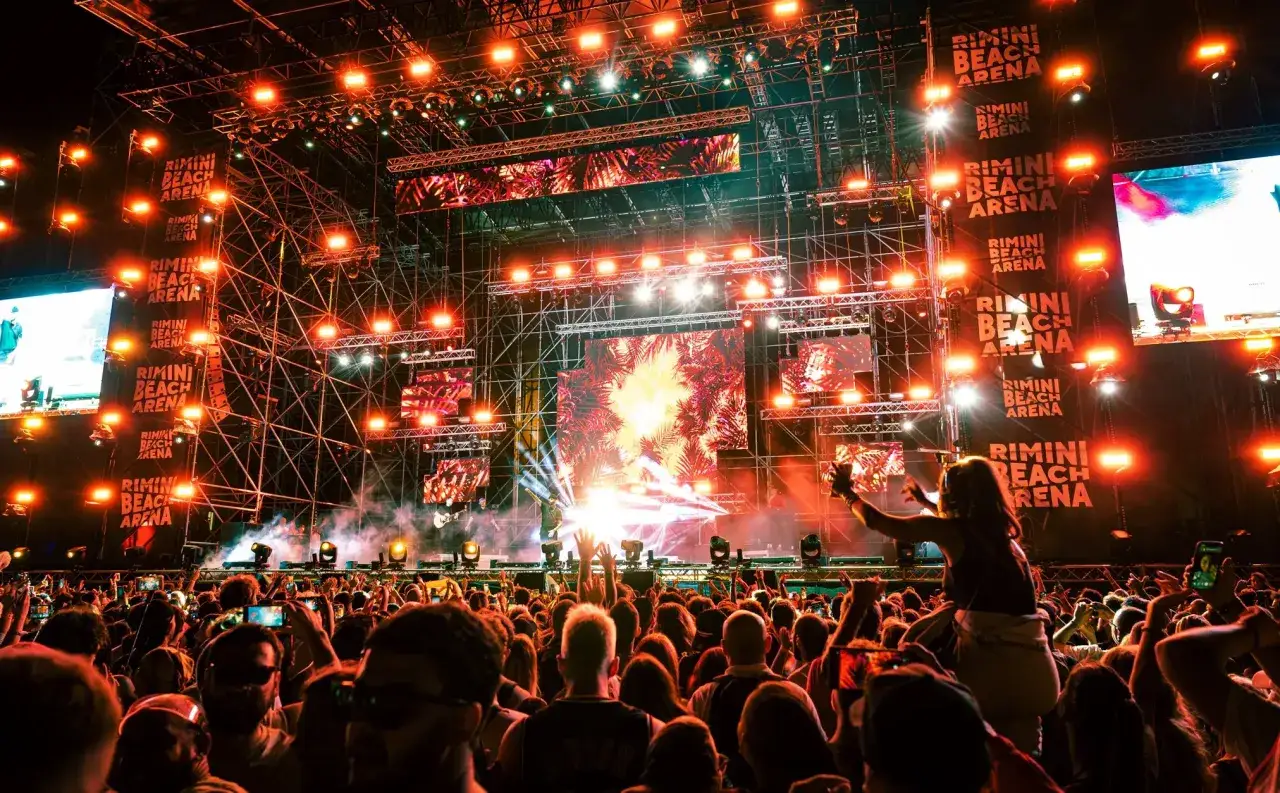 Un concerto elettrizzante al Rimini Beach Arena, con luci abbaglianti e una folla in festa.