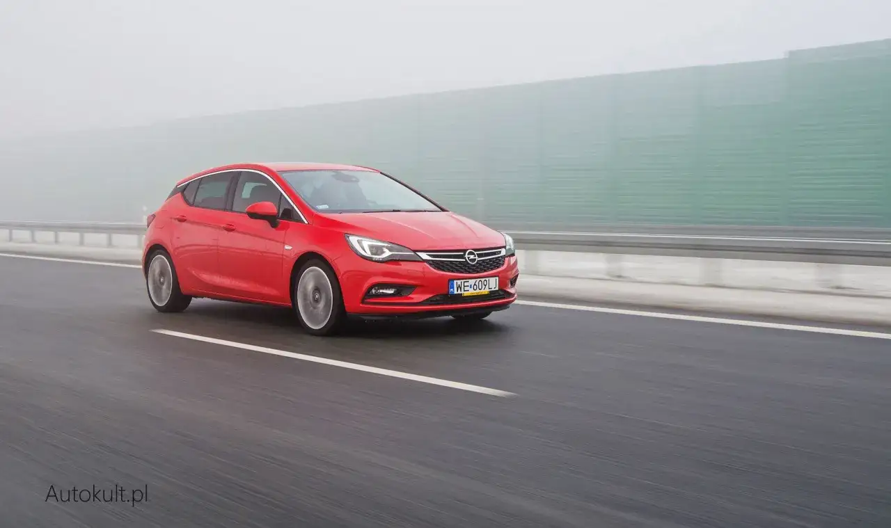 Czerwona Opel Astra jedzie autostradą we mgle. Zastanawiasz się, ile pali Opel Astra? Ten model może być zaskakująco oszczędny.