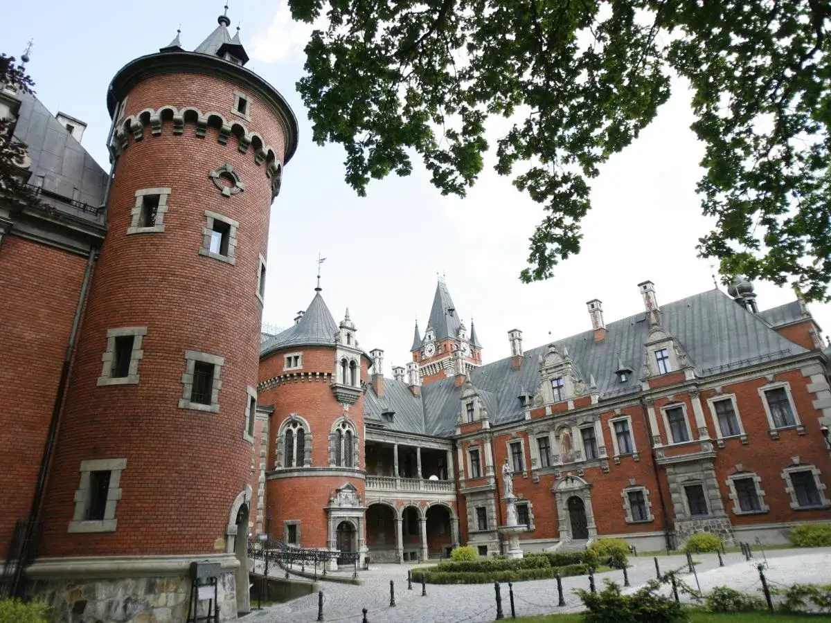 Pławniowice atrakcje: imponujący zamek z cegły z okrągłą wieżą i dziedzińcem, otoczony zielenią.