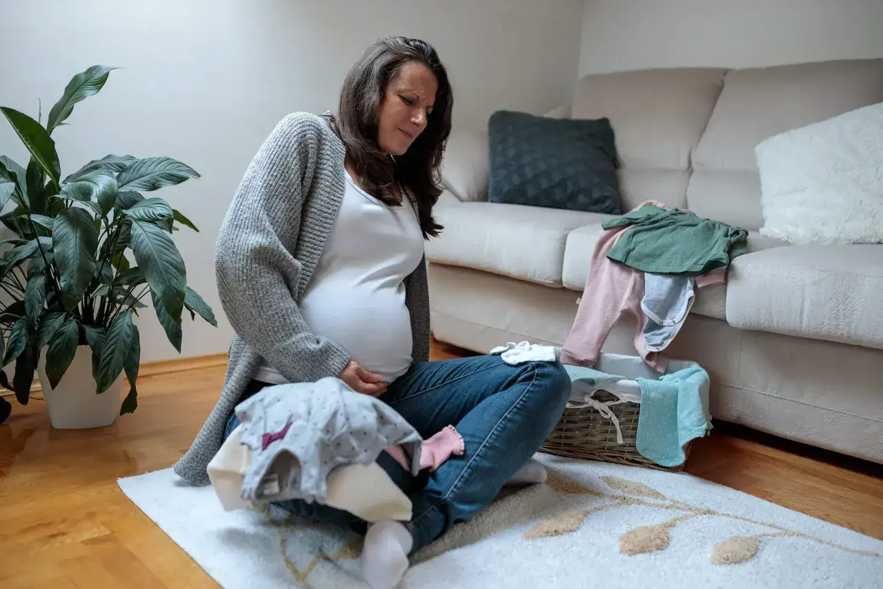 Schwangere Frau mit Babykleidung, die sich an den Bauch fasst, vielleicht wegen Braxton Hicks Kontraktionen.