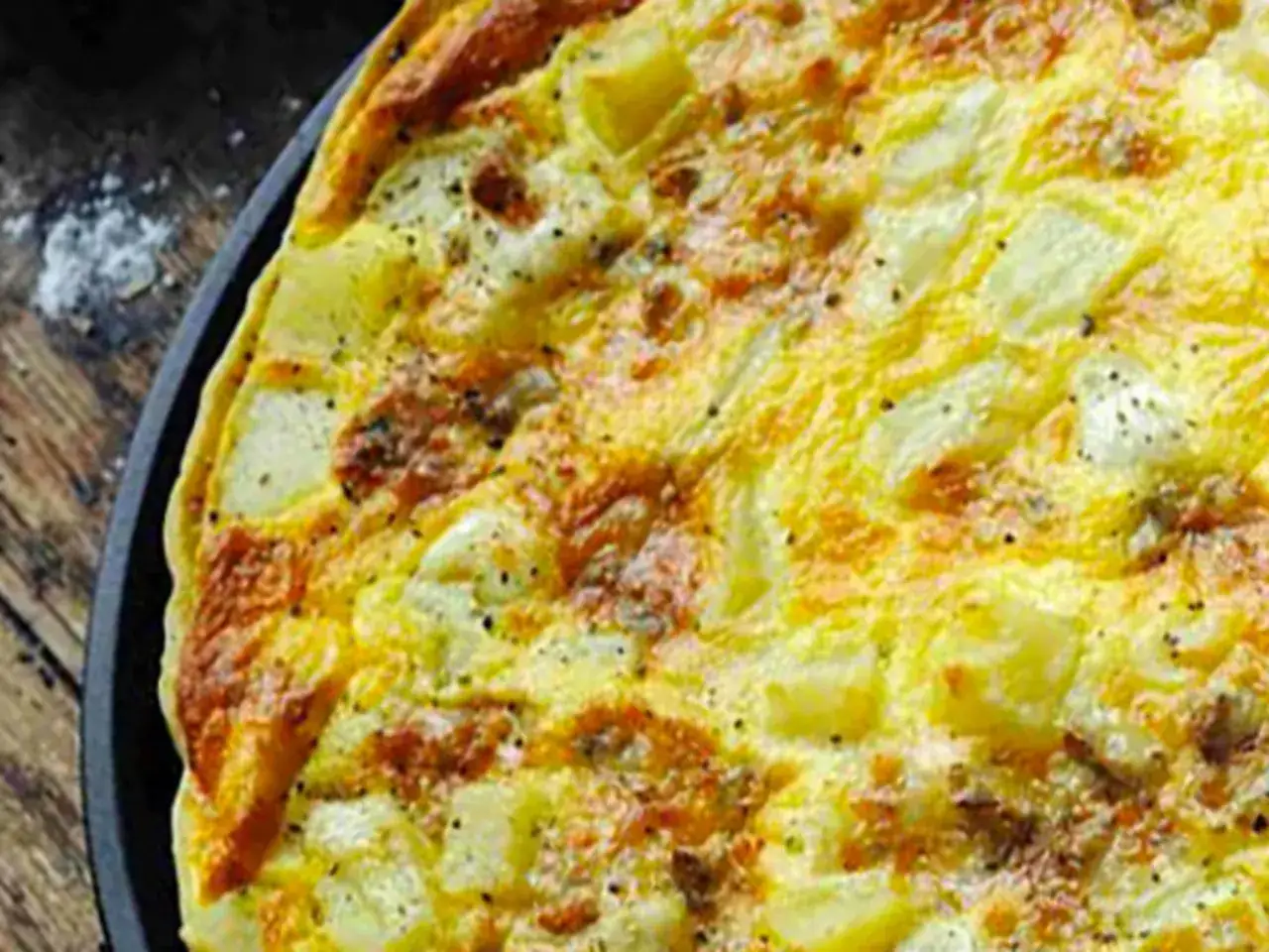 Une d&eacute;licieuse quiche au bleu, dor&eacute;e et parsem&eacute;e de poivre noir, avec des morceaux de pommes de terre visibles.