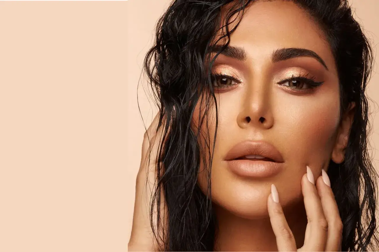 Un visage de femme avec un maquillage sophistiqu&eacute;, des yeux cuivr&eacute;s et des l&egrave;vres en teinte nude. Ses cheveux mouill&eacute;s encadrent son visage.