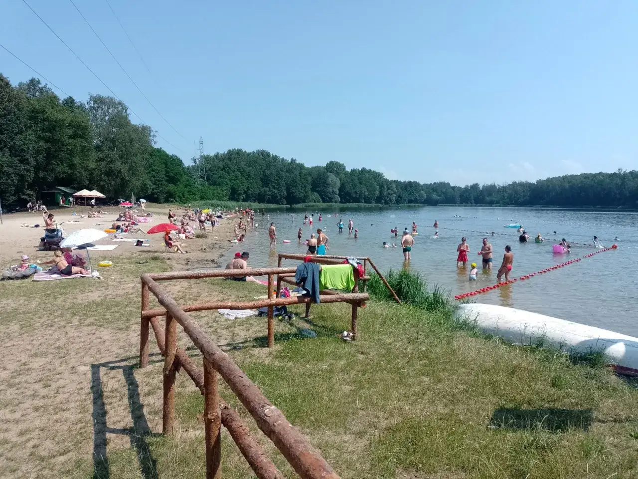 Słoneczny dzień nad jeziorem Rogoźnik. Ludzie kąpią się, opalają na plaży i odpoczywają w wodzie.