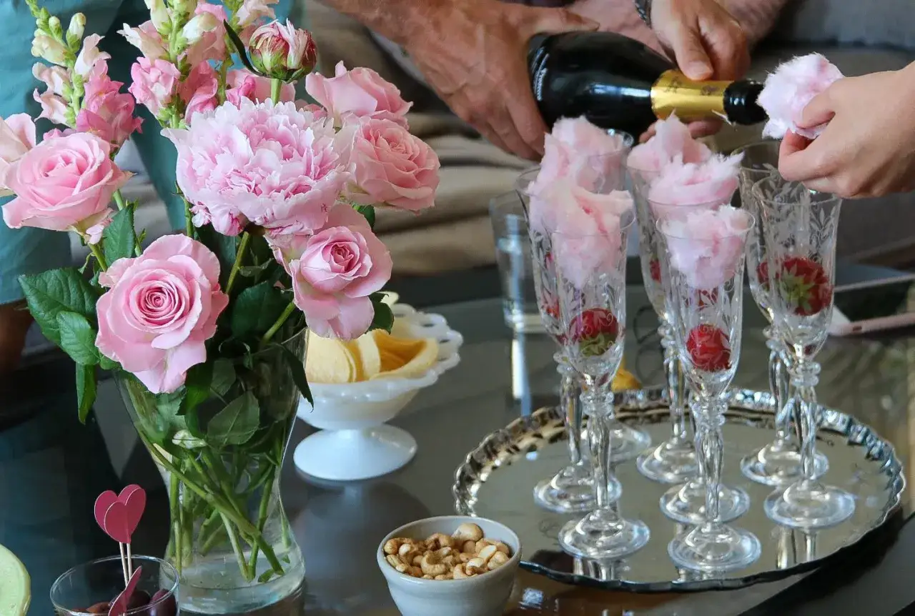 En vacker rosa dukning med blommor, jordgubbar och sockervadd i champagneglas. En festlig start p&aring; kv&auml;llen!