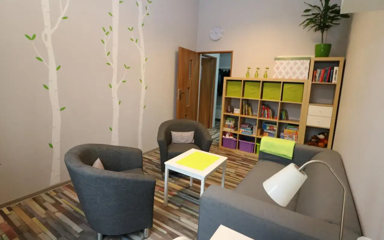 Przytulny pokój terapeutyczny z sofą, fotelami, regałem i dekoracjami ściennymi w kształcie drzew.