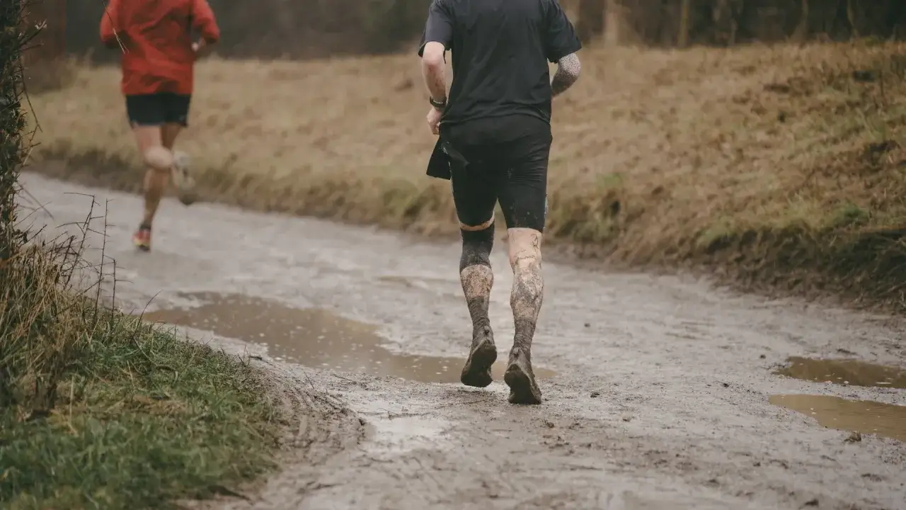 Zwei Läufer trotzen dem Wetter und joggen bei Regen durch matschiges Gelände.