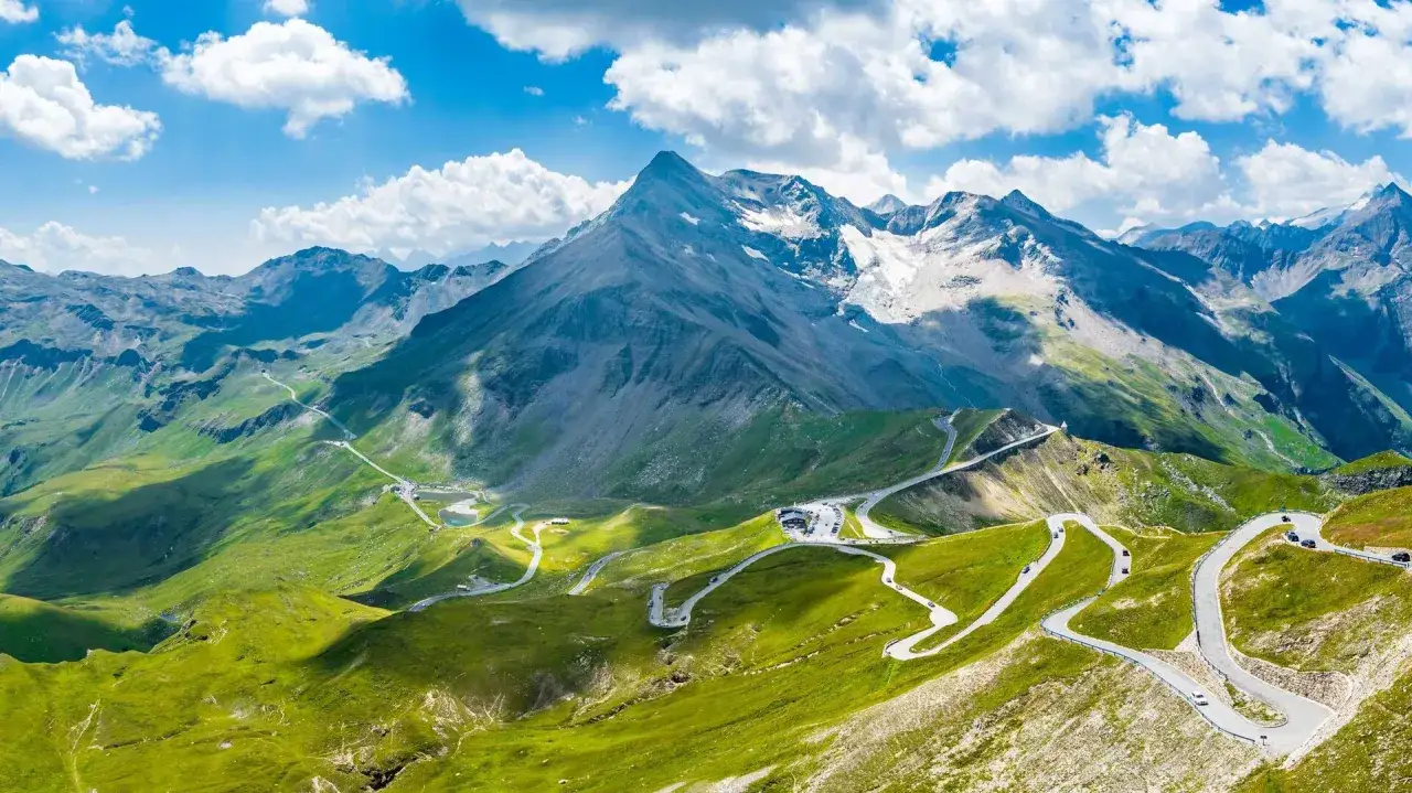 Widok na najwyższy szczyt w Austrii, Grossglockner, z krętą drogą i zielonymi zboczami.