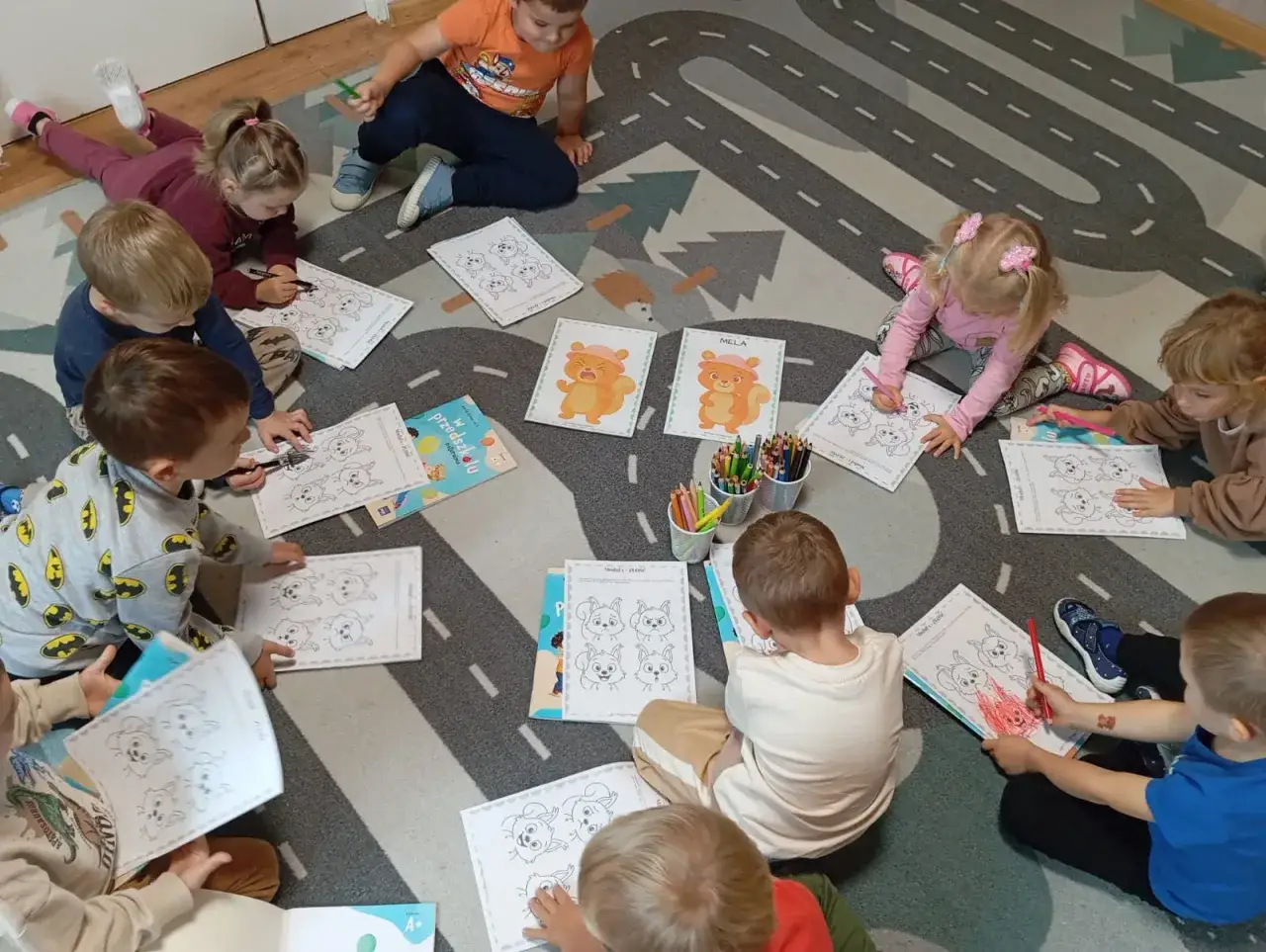 Dzieci na dywanie rysują zwierzątka. To jedne z tematów zajęć pedagoga szkolnego w szkole podstawowej, rozwijające kreatywność i zdolności manualne.
