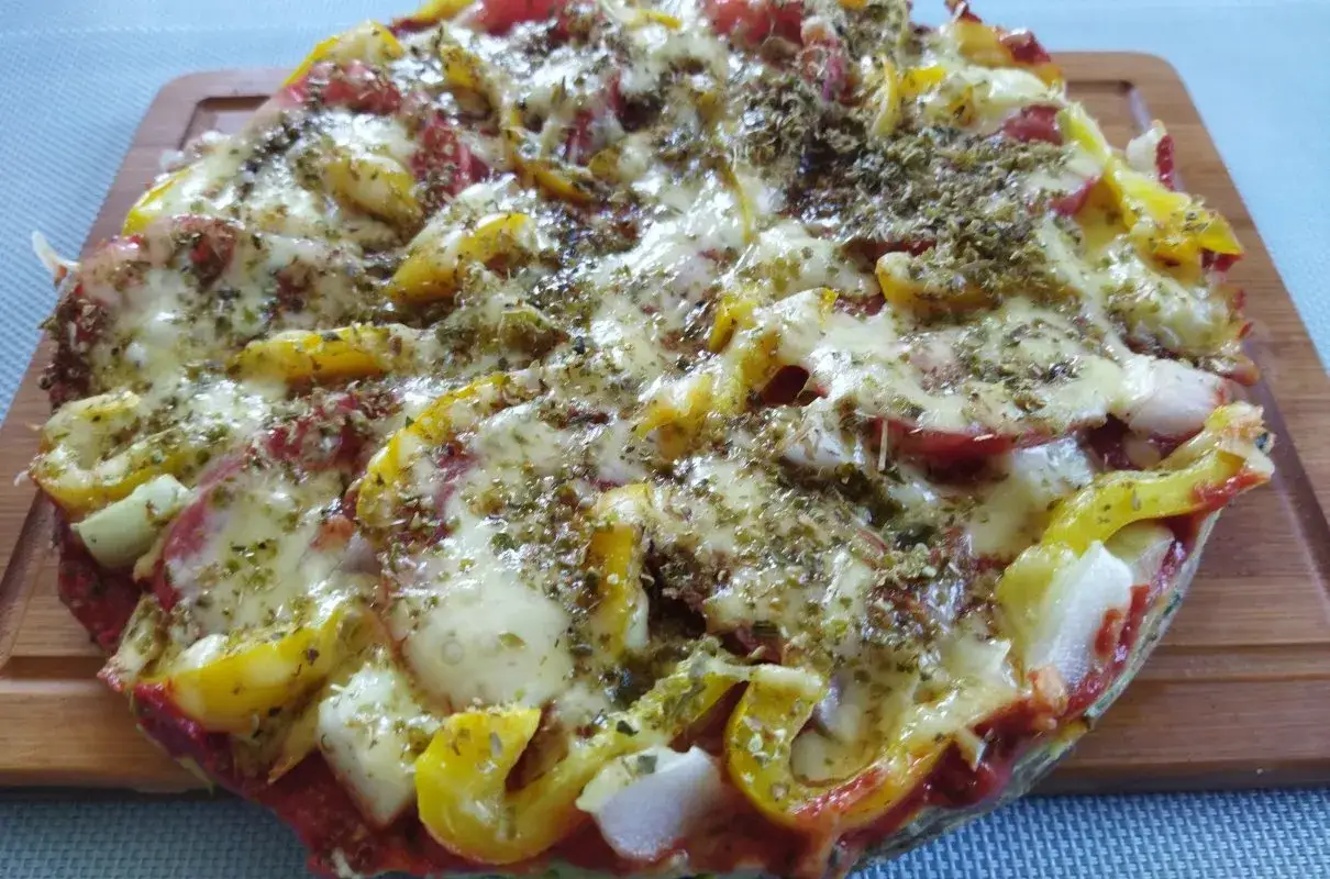 Pyszna pizza z cukinii z kolorową papryką i roztopionym serem, posypana ziołami.