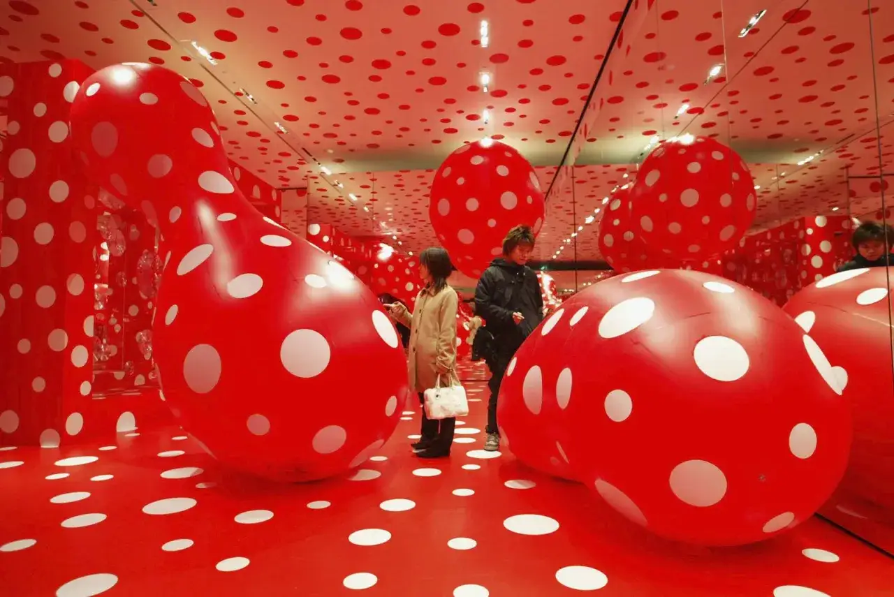 An immersive Yayoi Kusama installation with red and white polka dots. Giant inflatable polka-dotted sculptures fill the room, reflecting in mirrored walls.