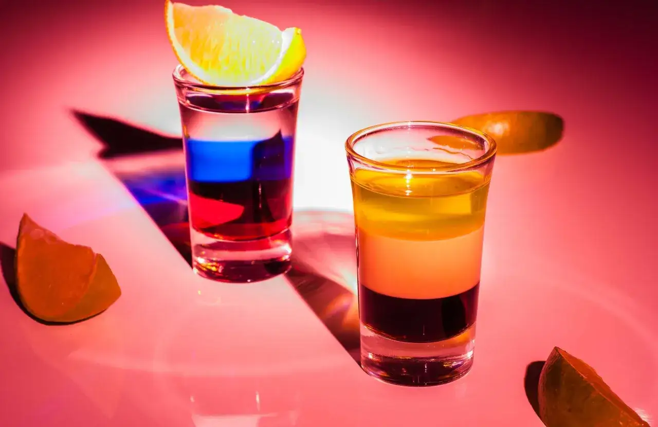 Dwa shoty warstwowe, jeden z cytryną, drugi z pomarańczą, prezentują kontrast między estetyką shotów warstwowych a mieszanych.