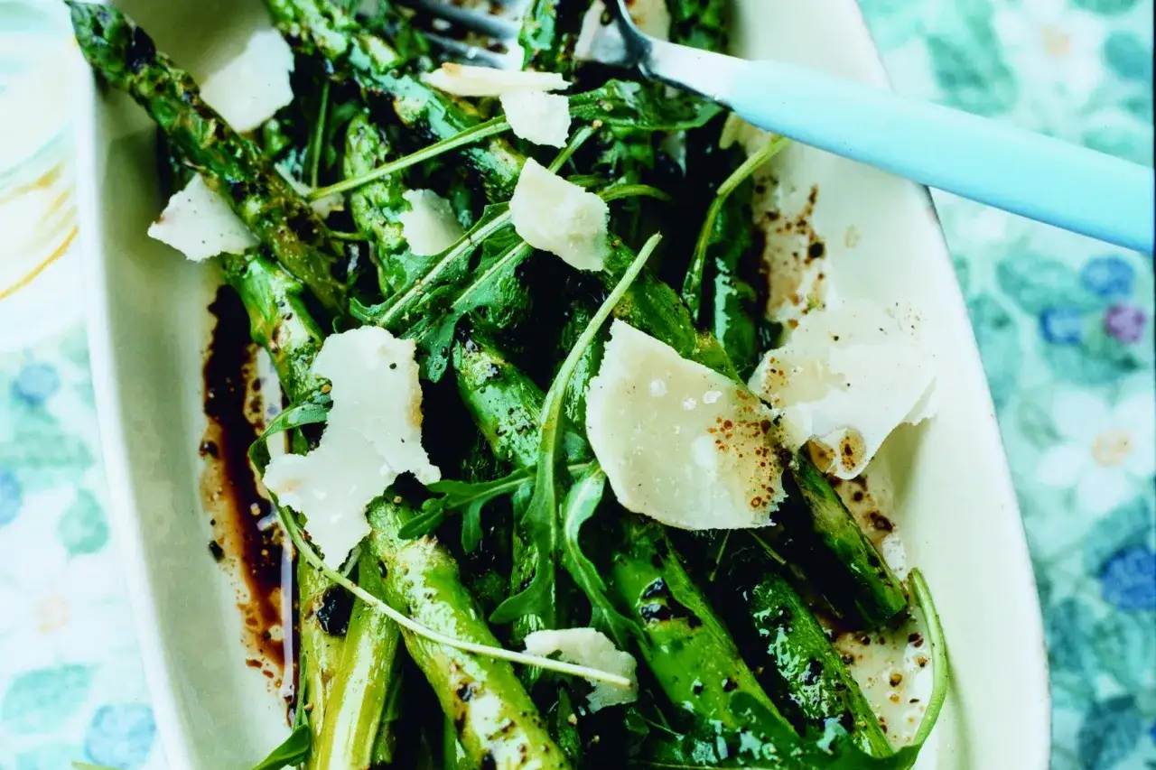 Grillad sparris med parmesan och ruccola, serverad i en vit sk&aring;l med en ljusbl&aring; gaffel.