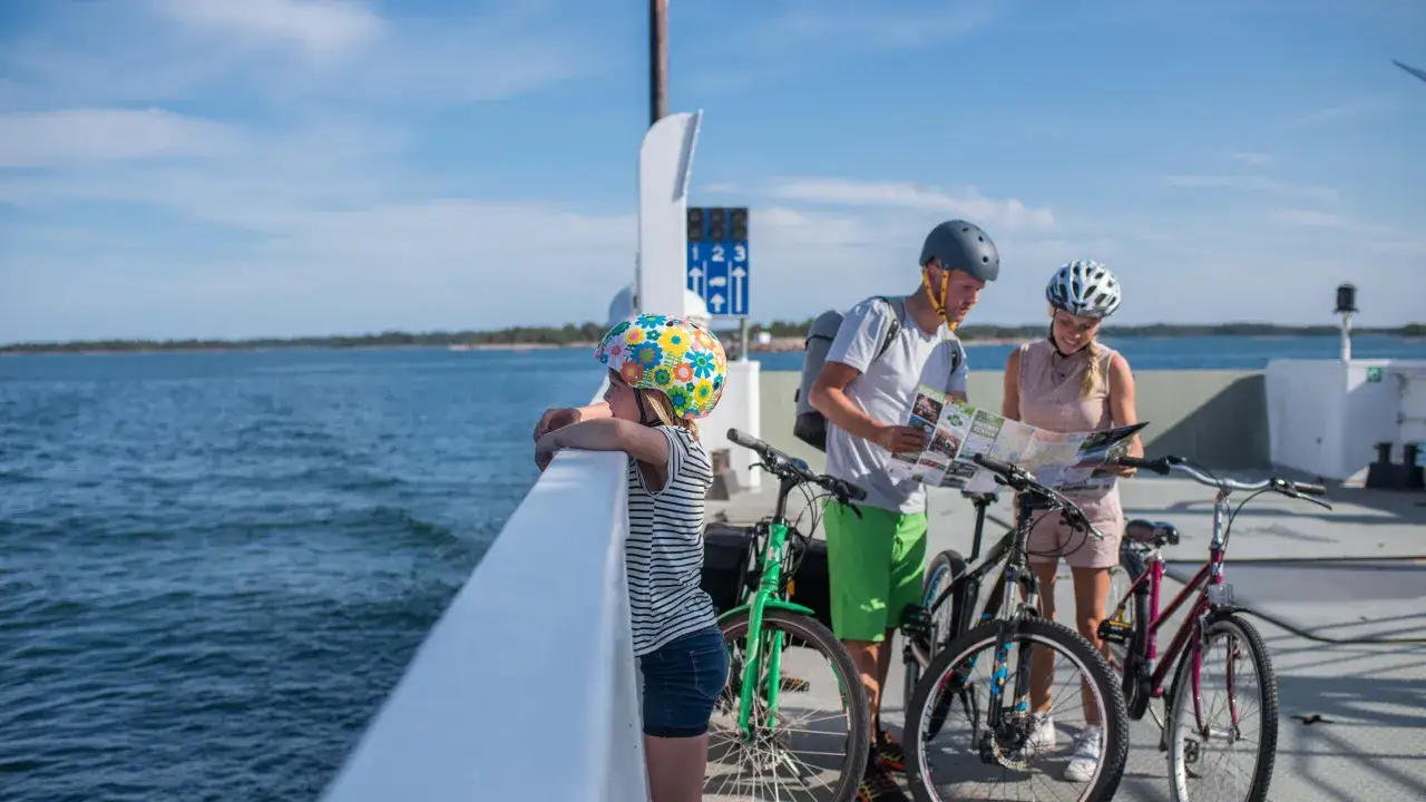 Familj med cyklar p&aring; en f&auml;rja, planerar sin resa till &Aring;land med karta.