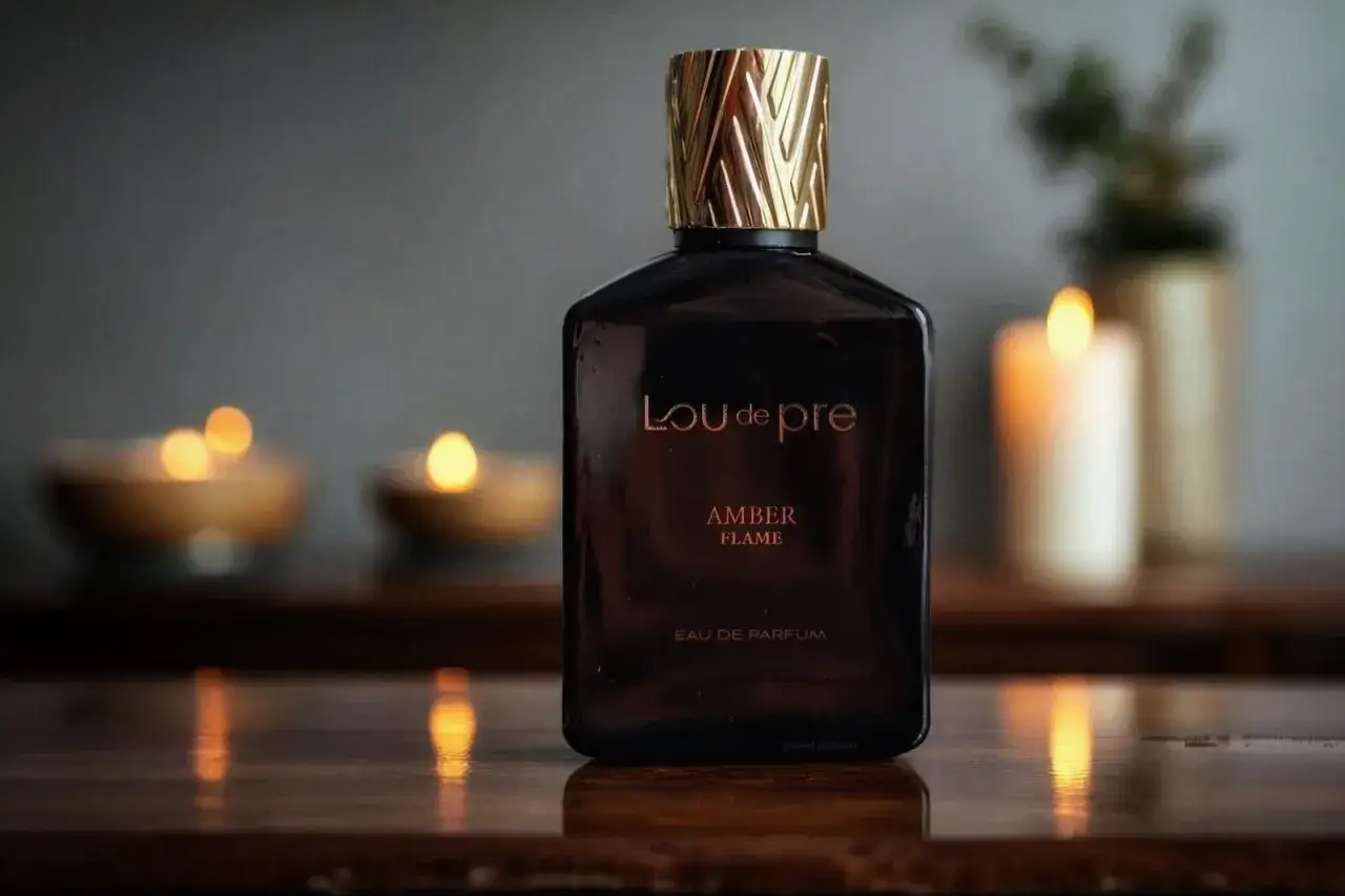 Elegancka butelka perfum Lou de Pre Amber Flame, otoczona ciepłym blaskiem świec, tworzy atmosferę luksusu i tajemniczości.