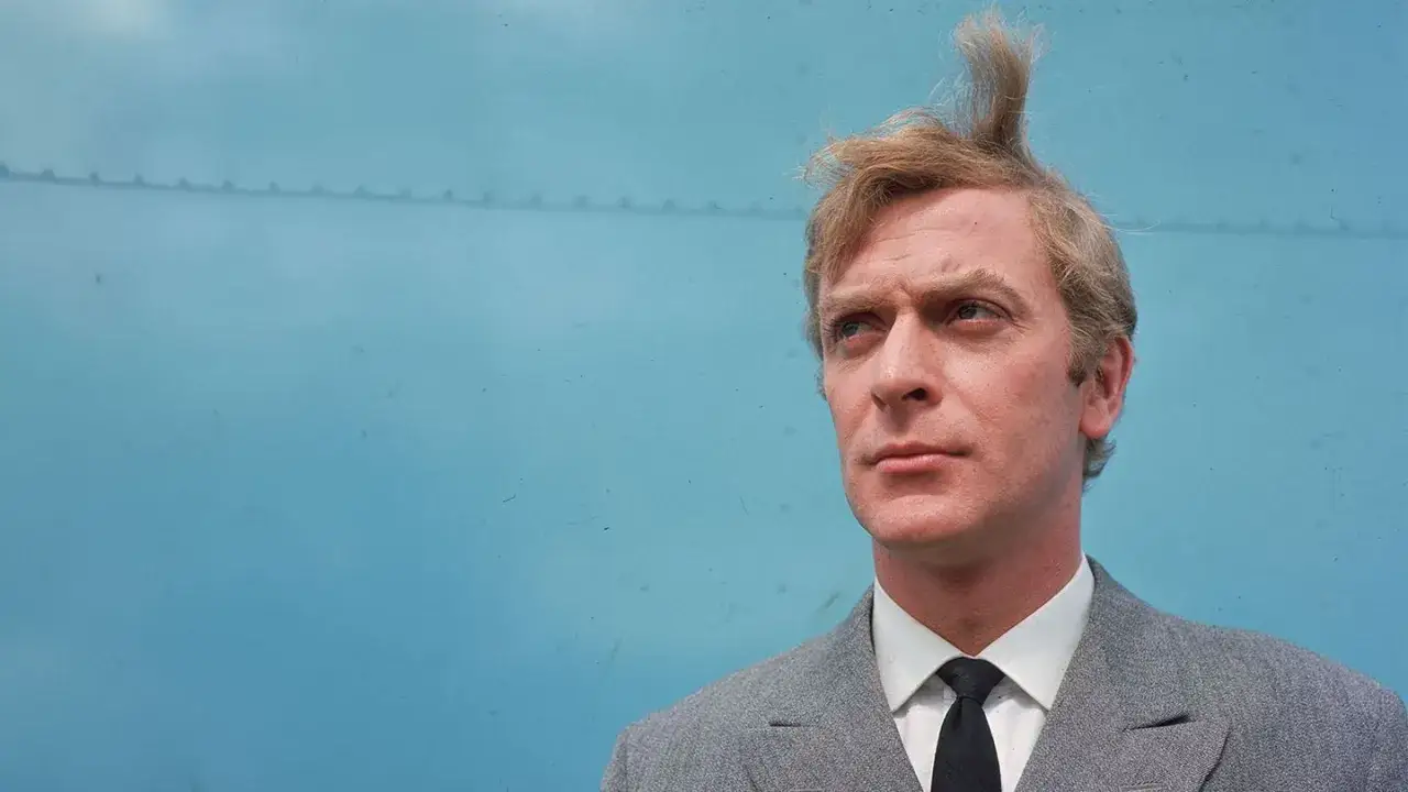 Michael Caine w szarym garniturze i z charakterystyczną fryzurą, jak z jego kultowych filmów.