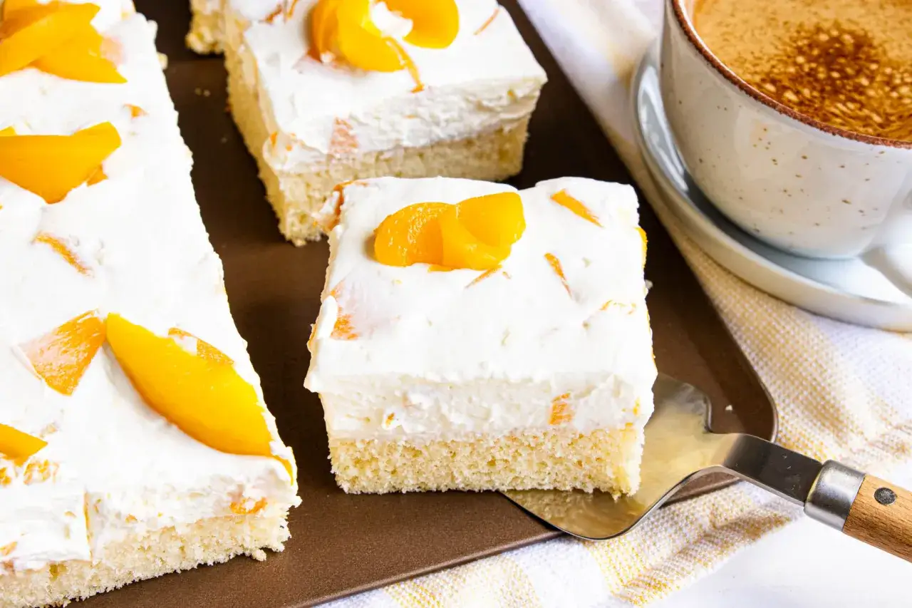 Saftiger Pfirsich Schmand Kuchen mit frischen Pfirsichstücken und einer cremigen Schicht, bereit zum Servieren neben einer Tasse Kaffee.