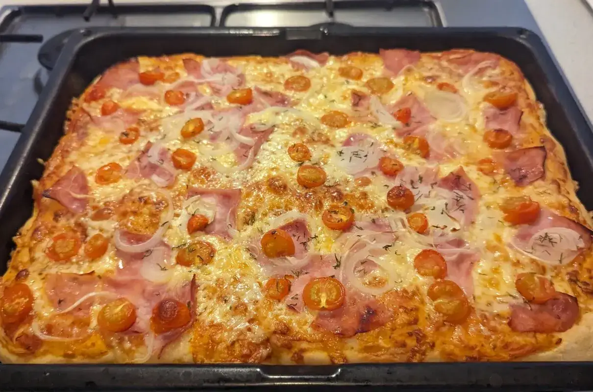 Pyszna, domowa pizza z szynką, pomidorkami koktajlowymi i cebulą, prosto z pieca.
