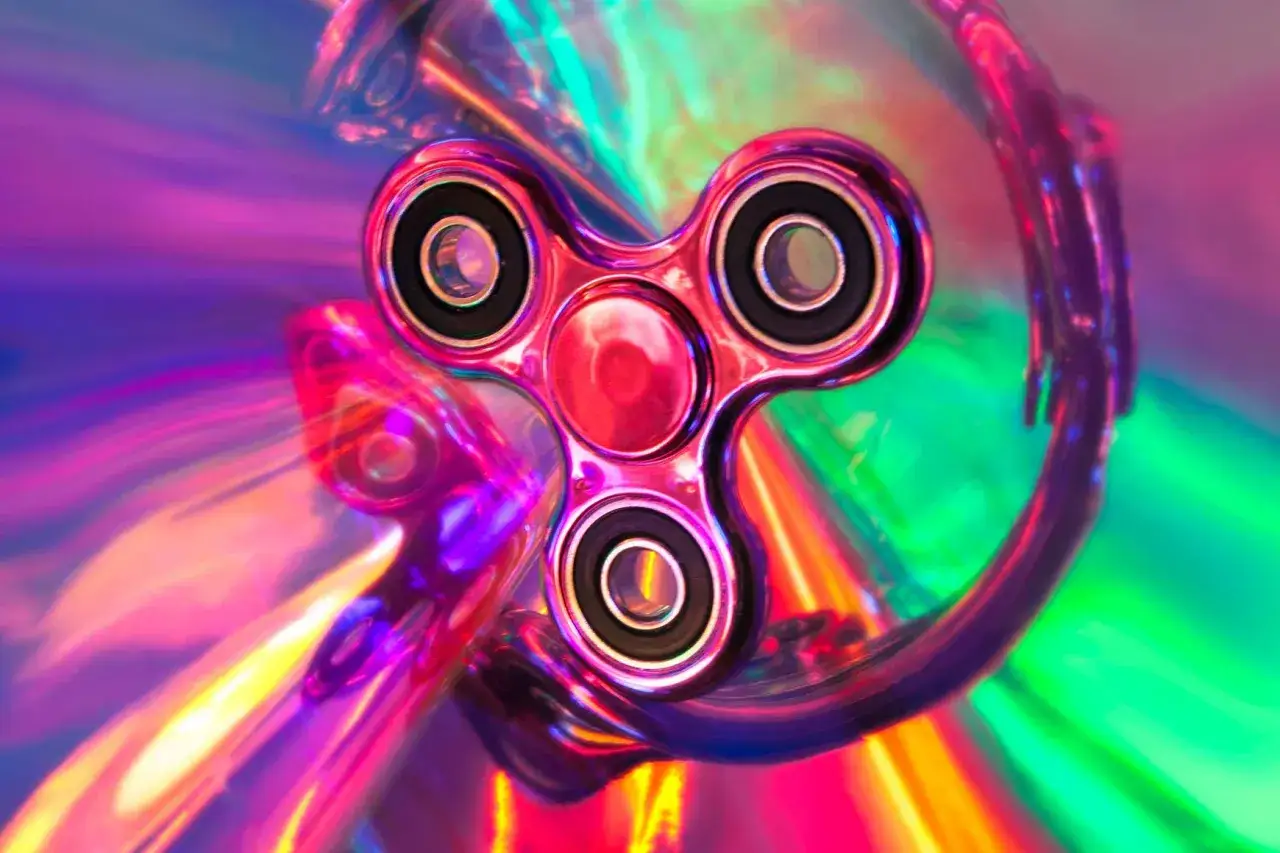 En glänsande fidget spinner i regnbågens alla färger, fångad i ett virvlande ljusspel.