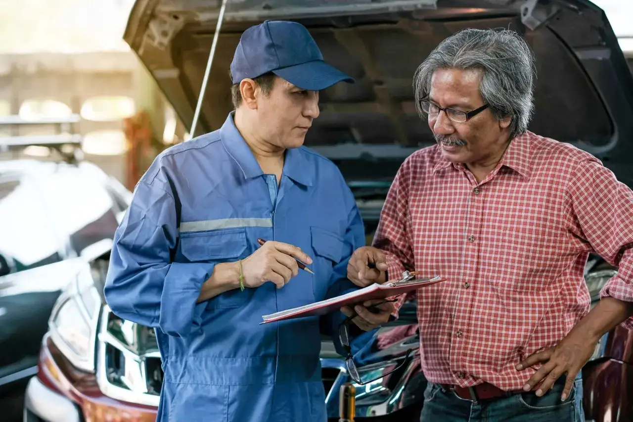 Un client discute avec un mécanicien devant une voiture. Il semble qu'il veuille porter plainte contre un garage automobile.