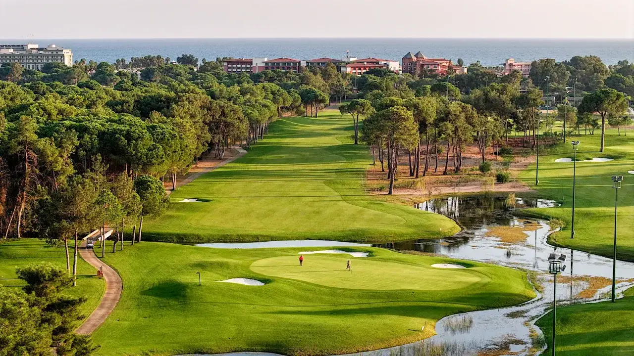 Vacker golfbana i Belek med gröna fairways, vattenhinder och pinjeträd. Två spelare njuter av en runda golf.