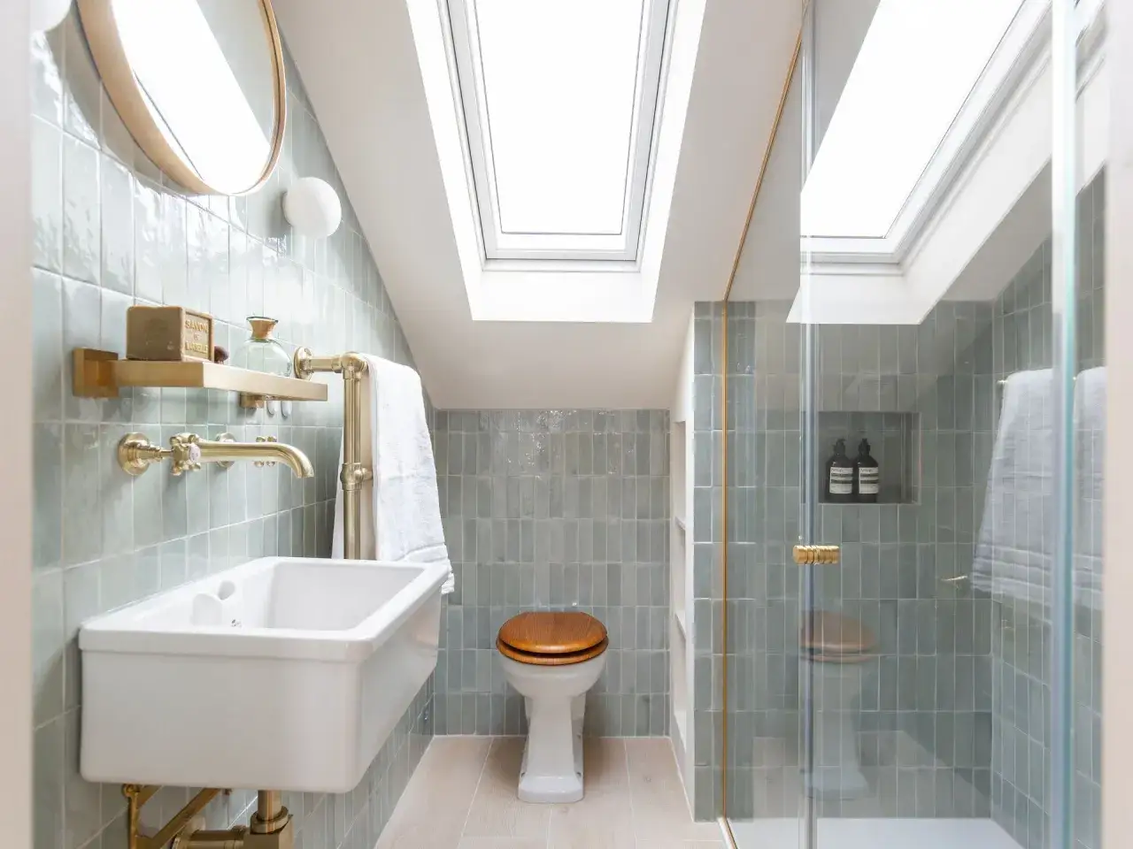 Elegantes mini aseos de cortesía con ducha, lavabo y WC, revestidos de azulejos verde menta y remates dorados.
