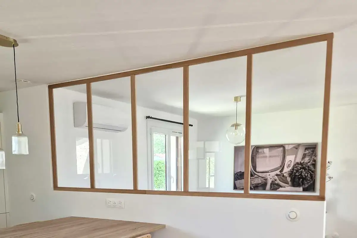 Une verri&egrave;re en bois, moderne et &eacute;pur&eacute;e, s&eacute;pare les espaces. Elle refl&egrave;te une pi&egrave;ce lumineuse avec une clim et une &oelig;uvre d'art.