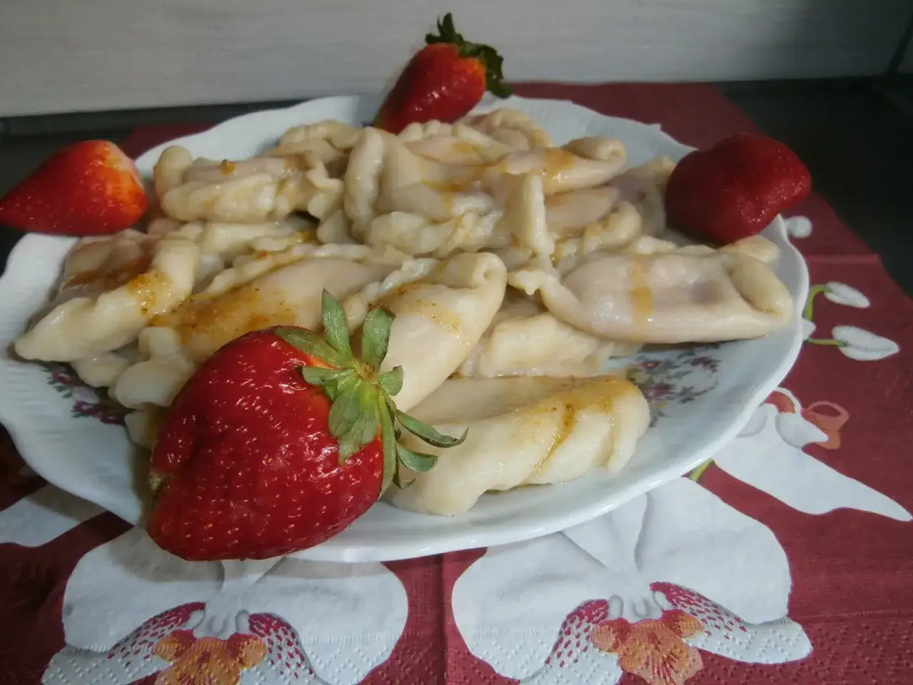 Talerz pełen pysznych, domowych pierogów z truskawkami, ozdobiony świeżymi owocami.