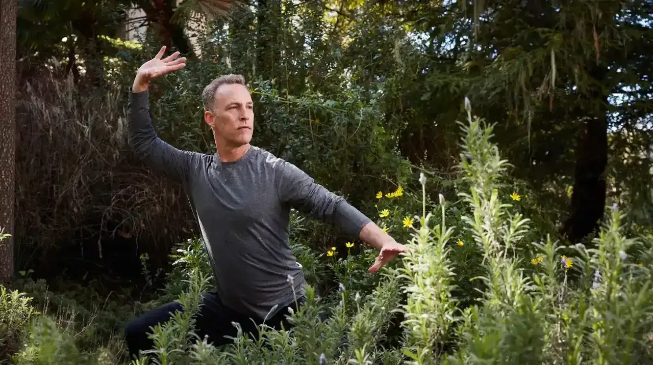 Mężczyzna ćwiczy qigong dla początkujących w otoczeniu zieleni i kwiatów.