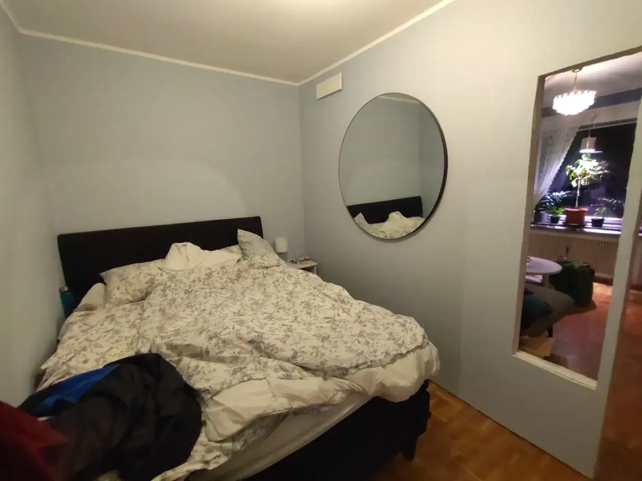 Sovrum med en stor s&auml;ng, spegel p&aring; v&auml;ggen och en &ouml;ppen d&ouml;rr som visar ett annat rum. K&auml;nns som d&aring;lig luft i sovrummet.