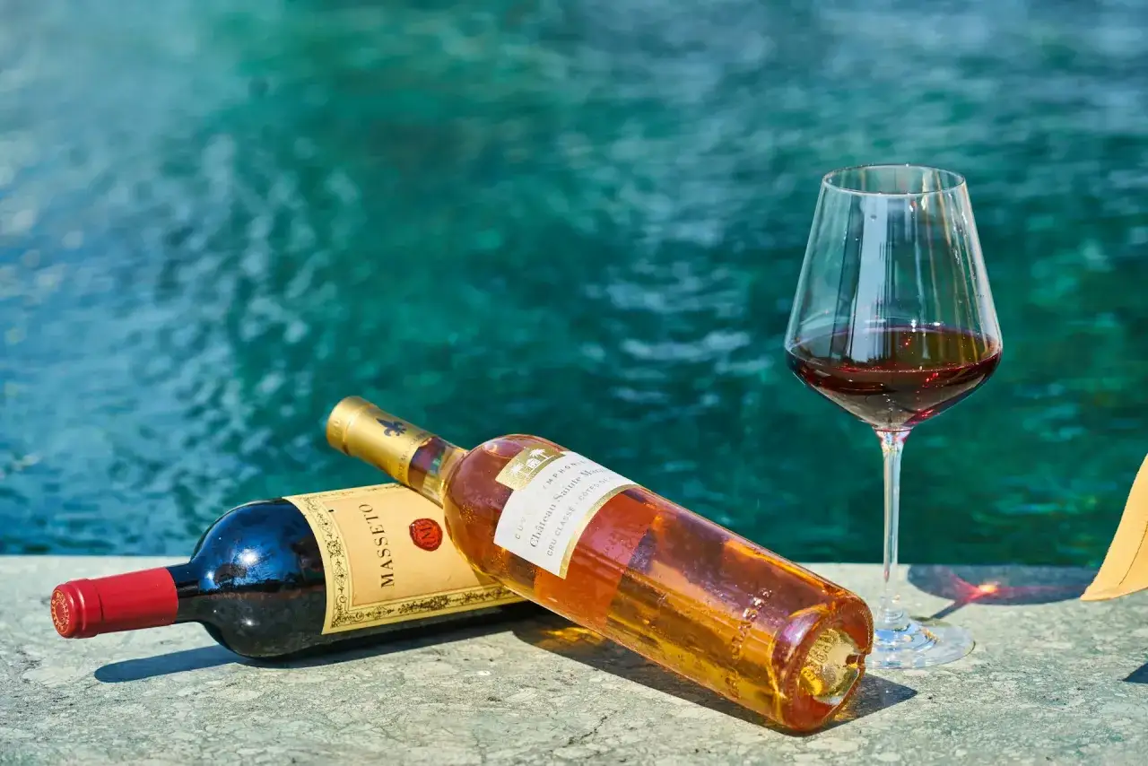 Zwei Flaschen Wein und ein Glas Rotwein im Sommer am Pool.