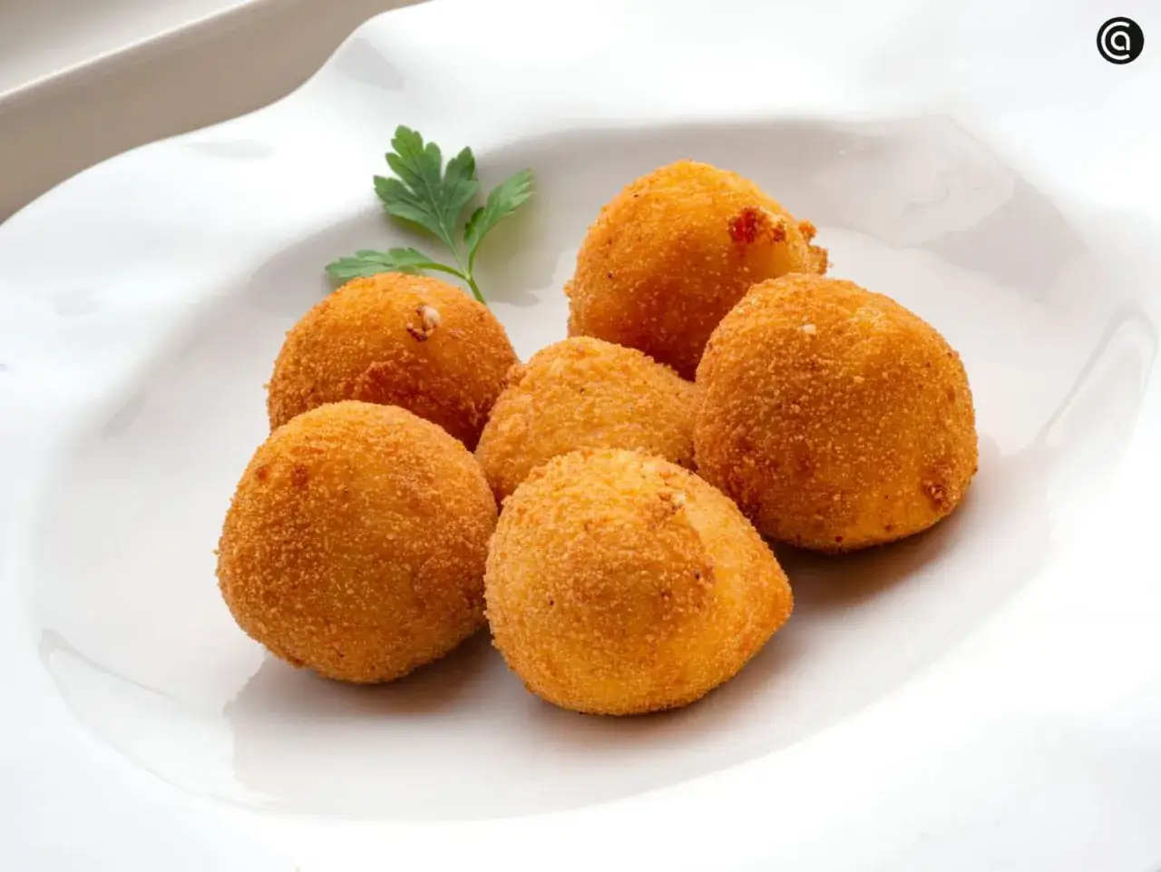 Seis croquetas de gambas doradas y crujientes, servidas en un plato blanco con una ramita de perejil.