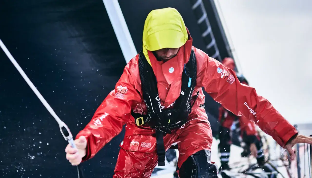 Un velista con giacca rossa e cappuccio giallo, pronto a navigare. Ecco come vestirsi in barca a vela per affrontare il mare.