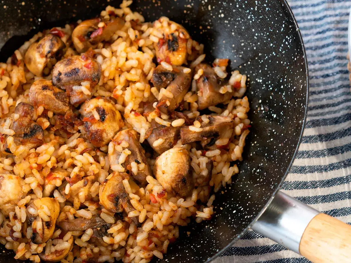 Arroz con champi&ntilde;ones reci&eacute;n hecho en sart&eacute;n, con trozos dorados y sabrosos.