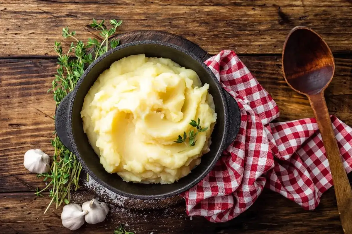 Puszyste puree ziemniaczane w misce, obok czosnek i zioła. Czy można jeść ziemniaki przed kolonoskopią? Zależy od zaleceń lekarza.