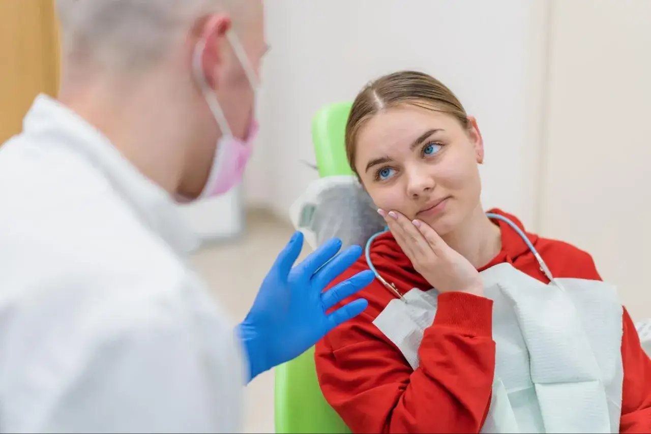 Dziewczyna z bólem zęba u dentysty, który proponuje tabletki na ból zęba.