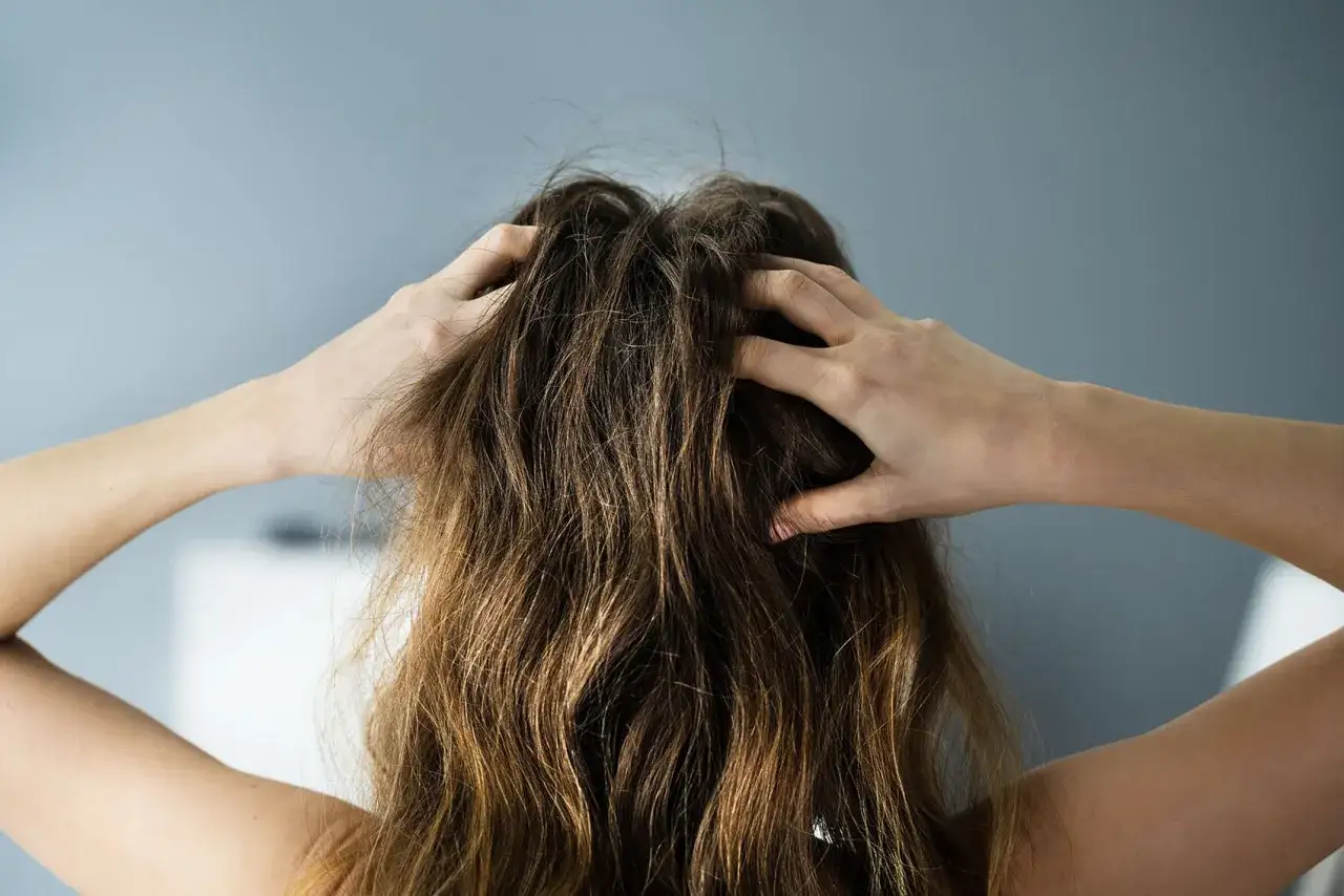 Mains grattant des cheveux emmêlés, peut-être à cause d'un shampoing sec Batiste dangereux.