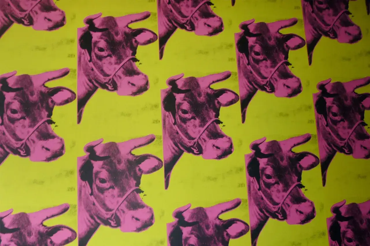 A repeating pattern of pink cow heads on a yellow background, reminiscent of 80s artists like Andy Warhol.