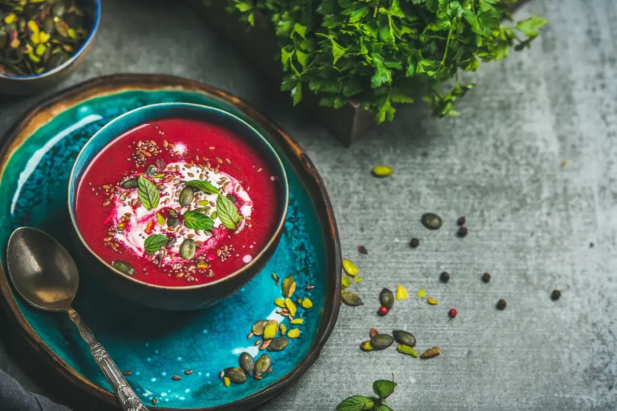Soupe de betterave rouge polonaise, garnie de crème, de graines et de menthe, servie sur une assiette bleue vibrante.