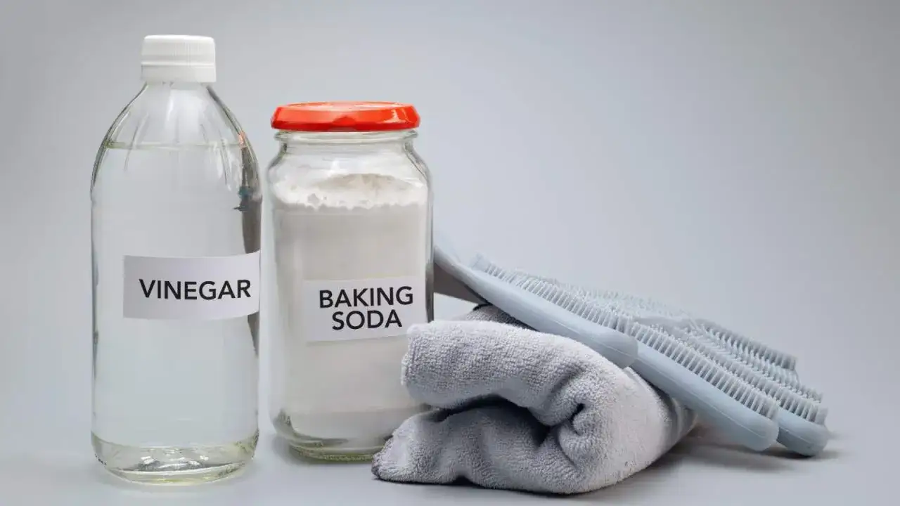 Botella de vinagre y frasco de bicarbonato de sodio junto a un paño y cepillos, listos para una limpieza ecológica.