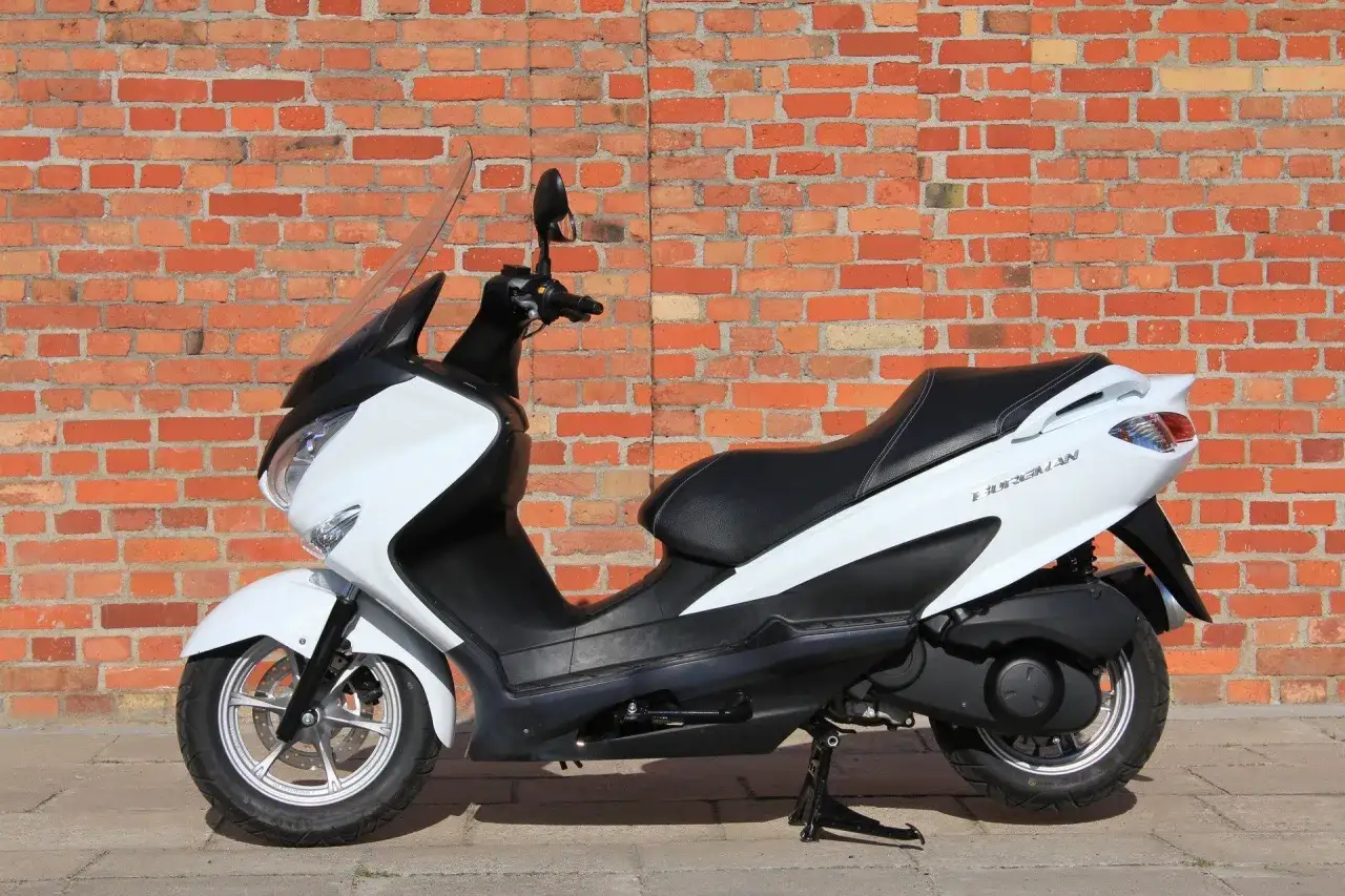 Biały skuter Suzuki Burgman 125 na tle ceglanej ściany. Sprawdź suzuki burgman 125 dane techniczne.