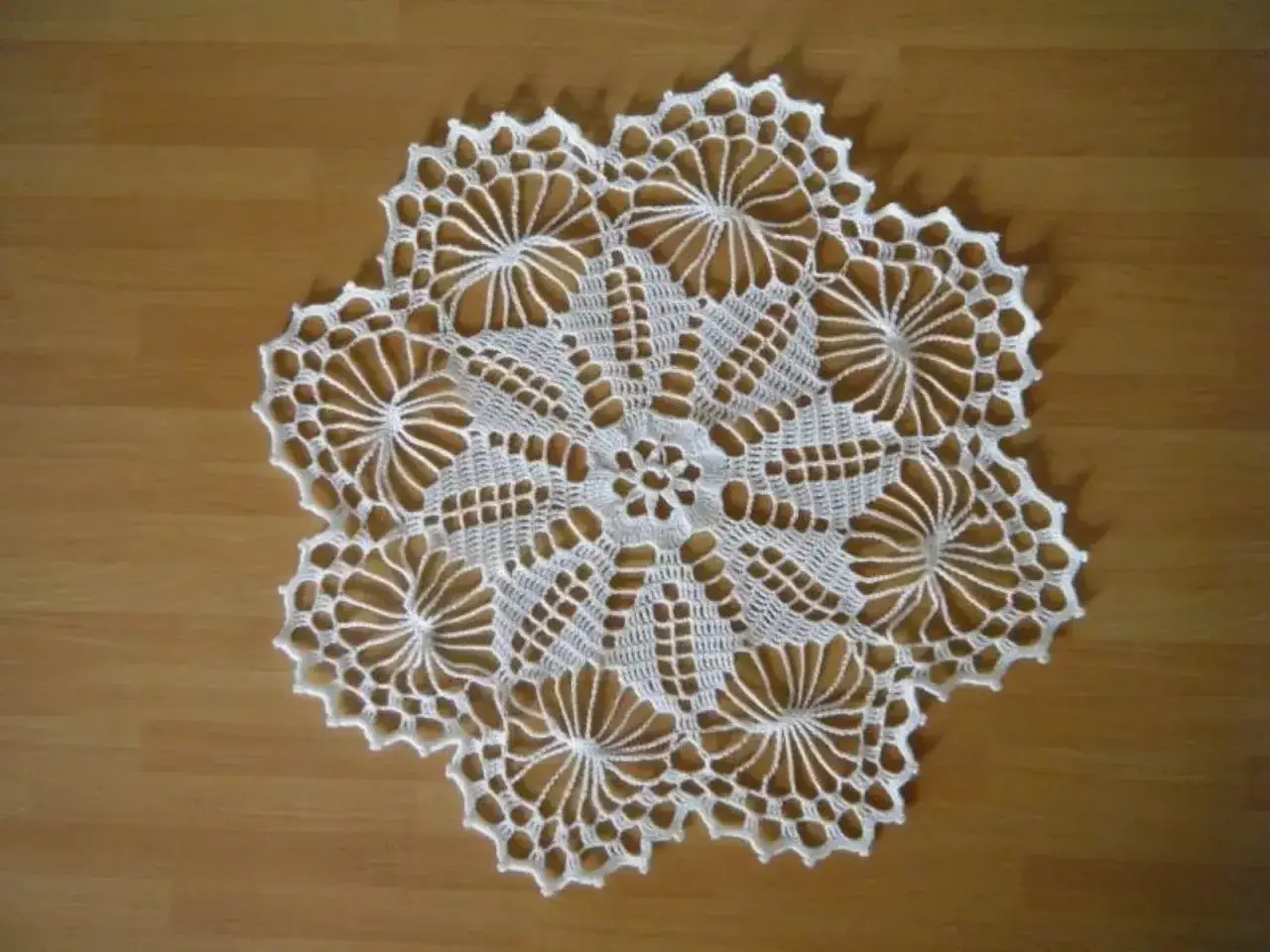 Un centrino all'uncinetto bianco, con motivi floreali e geometrici, adorna un mobile in legno. Dimostra che si usano ancora i centrini sui mobili.
