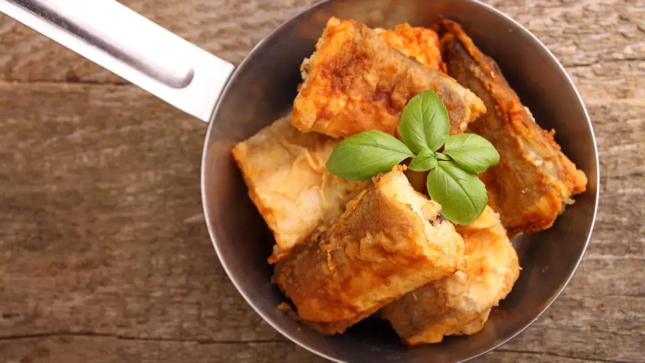 Gebratener Seehecht mit Haut in einer Pfanne, garniert mit Basilikum. Perfekt zubereitet für ein köstliches Essen.