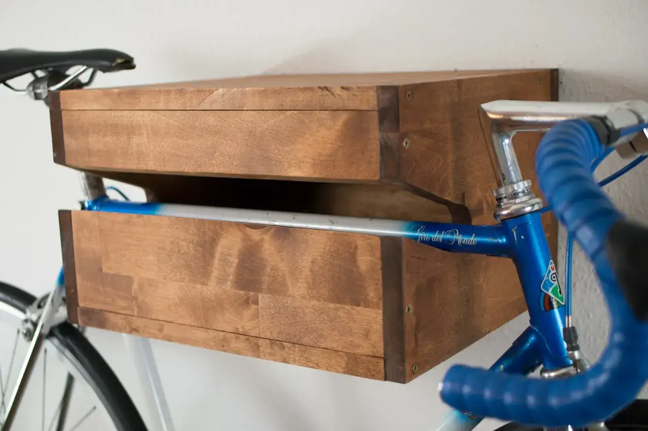 Holz-Fahrrad-Wandhalterung, die man selber bauen kann. Ein blaues Rennrad h&auml;ngt darin, Sattel oben, Lenker und Rahmen sichtbar.