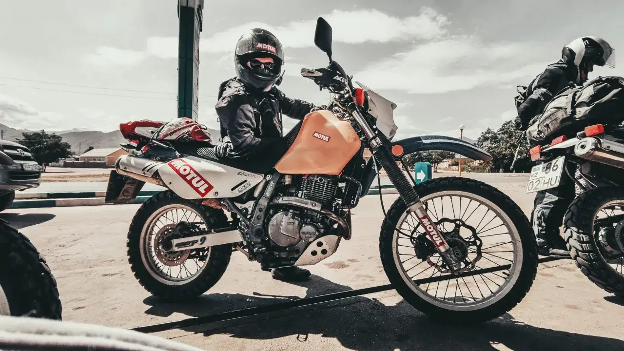 Motocyklista w kasku na pomarańczowym Suzuki DR650, gotowy do podróży.