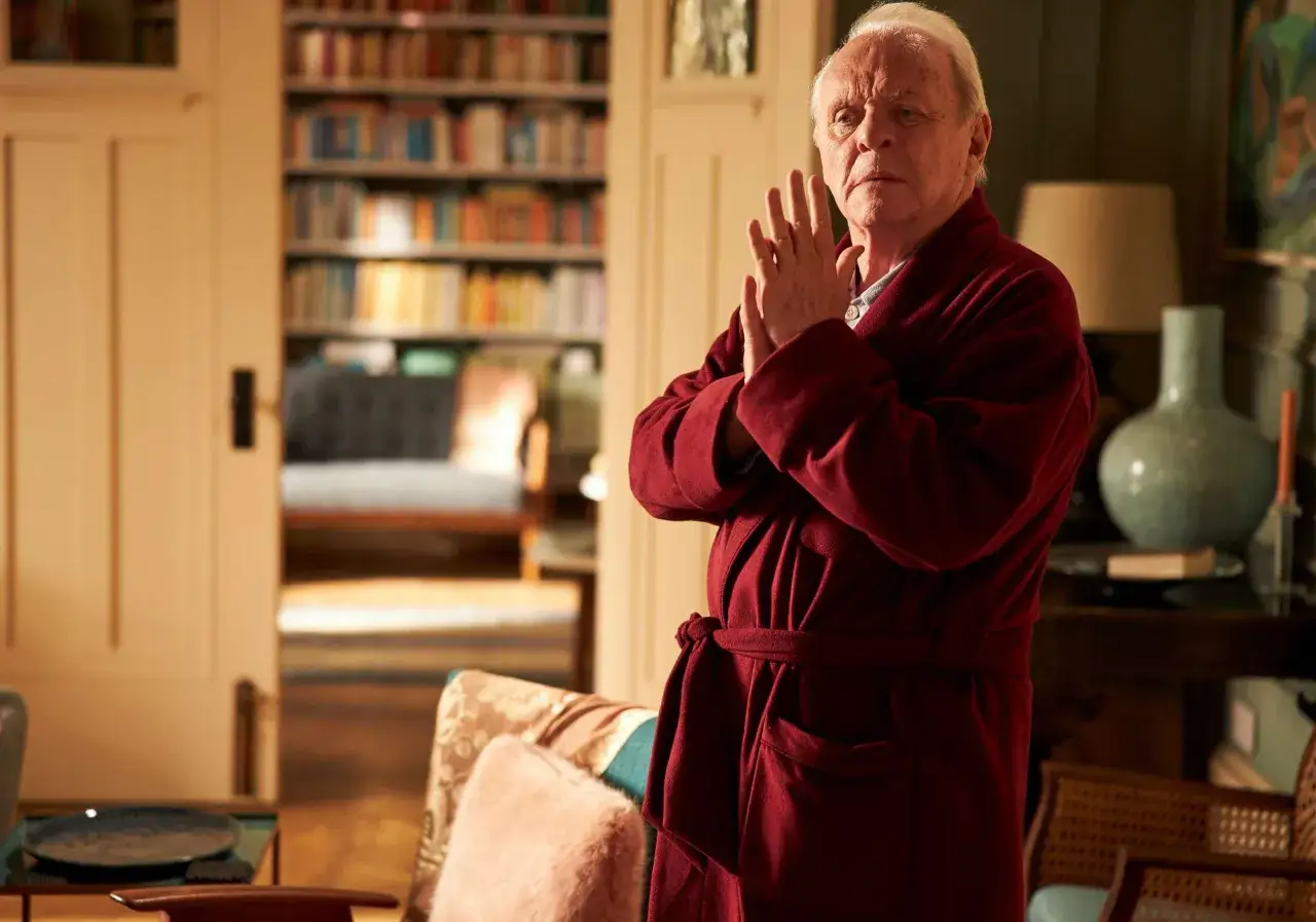 Anthony Hopkins i sin vinröda morgonrock, med händerna knäppta, i ett rum med bokhyllor. En gripande skildring av Anthony Hopkins demens.
